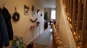 Warm fairy lights wrap around a wooden stair railing in a narrow home entry, showcasing simple ideas for decorating a hallway for christmas.